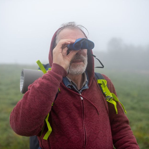 Man in red hoodie looks through binoculars outside