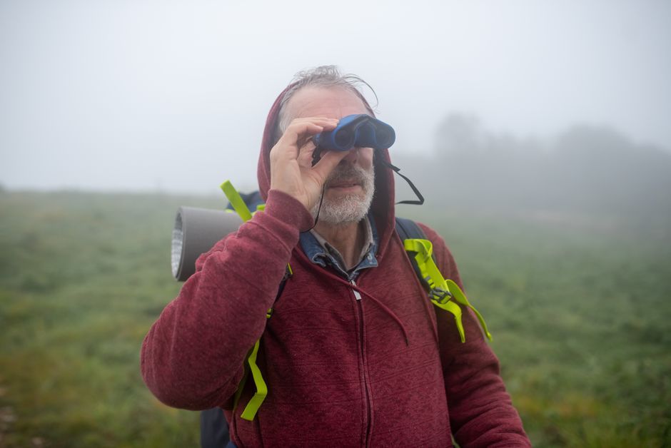 Man in red hoodie looks through binoculars outside