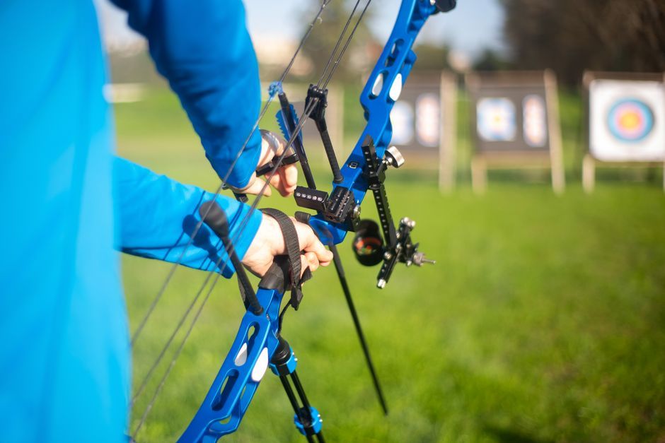 Person aiming blue compound bow at targets