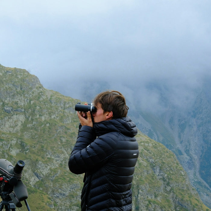 Hiker looking through binoculars at misty mountains